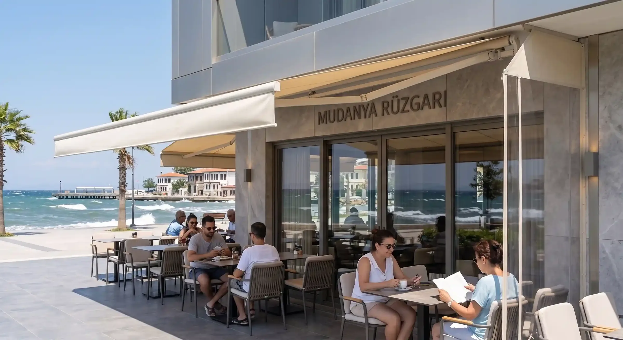 Tenda sa zglobnim rukama nad terasom kafića uz more — gosti sjede u hladu